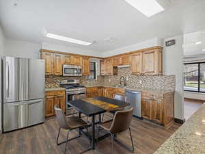 Kitchen featuring stainless steel appliances, wood finish cabinets, dark wood-style floors, and backsplash