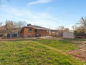 Back of property featuring a fenced backyard, brick siding, a patio, and a storage unit