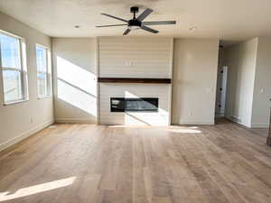 Unfurnished living room with light wood-style floors, ceiling fan, a large fireplace, and a textured ceiling