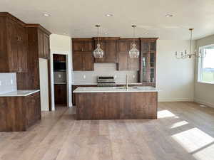 Kitchen featuring tasteful backsplash, light stone counters, dark wood finish cabinets, suspended lighting, and gas range