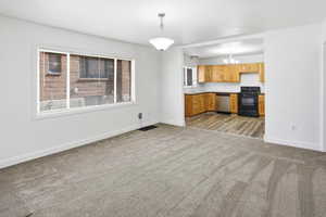 Kitchen featuring black / electric stove, dishwasher, hanging lights, light carpet, and open floor plan