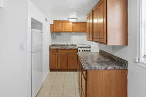 Kitchen featuring a textured wall, wood finish cabinets, dark countertops, white appliances, and a textured ceiling