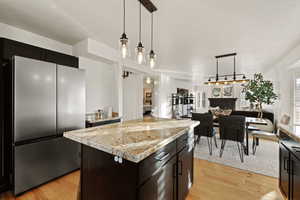 Kitchen with dark cabinetry, freestanding refrigerator, decorative light fixtures, and open floor plan