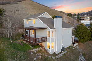 Back of property at dusk featuring a deck with mountain view, a shingled roof, and a chimney
