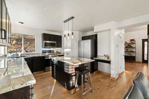 Kitchen featuring stainless steel appliances, a kitchen island, light wood-style flooring, light stone countertops, and decorative light fixtures