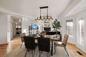 Dining space with a lit fireplace, light wood-type flooring, and a ceiling fan