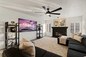 Living room featuring a glass covered fireplace, a ceiling fan, a textured ceiling, and carpet