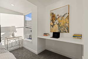 Office space featuring built in study area, dark colored carpet, and vaulted ceiling
