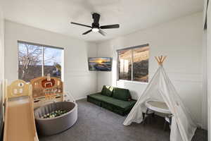 Recreation room with dark carpet, a textured ceiling, and ceiling fan