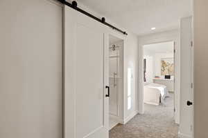 Hallway featuring a barn door, light carpet, a textured ceiling, and recessed lighting