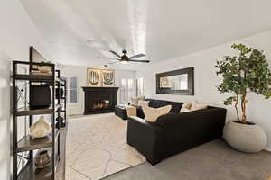 Living area with a warm lit fireplace, carpet, ceiling fan, and a textured ceiling