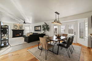 Dining space featuring a glass covered fireplace, light wood-style flooring, a textured ceiling, and a ceiling fan