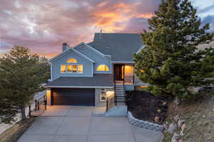 View of front of home with an attached garage, brick siding, a chimney, concrete driveway, and roof with shingles