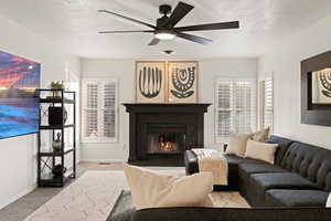 Carpeted living room featuring ceiling fan, a textured ceiling, and a glass covered fireplace