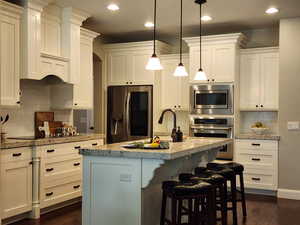 Kitchen with white cabinetry, stainless steel appliances, tasteful backsplash, an island with sink, and dark wood-style flooring