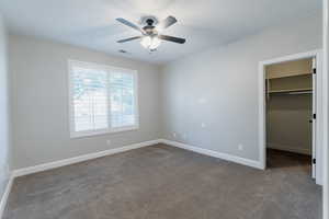 Unfurnished bedroom with dark carpet, a spacious closet, and ceiling fan