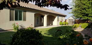 Back of property with a patio area, stucco siding, a storage unit, and a tile roof