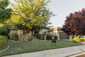 View of front of home featuring stone siding, a front yard, an attached garage, stucco siding, and concrete driveway