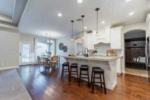 Kitchen featuring a kitchen island with sink, a breakfast bar area, dark wood-style floors, and white cabinetry