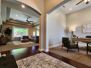 Office space featuring a ceiling fan, dark wood finished floors, recessed lighting, a raised ceiling, and arched walkways