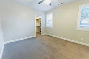 Unfurnished bedroom with a spacious closet, carpet floors, and a ceiling fan