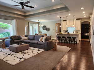 Living room with arched walkways, a tray ceiling, ceiling fan, dark wood-style floors, and hanging lights
