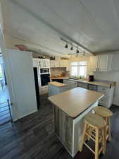 Kitchen with a center island, white cabinetry, light countertops, dark wood-style flooring, and rail lighting
