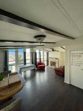 Living area with beamed ceiling, a glass covered fireplace, a ceiling fan, and wood finished floors