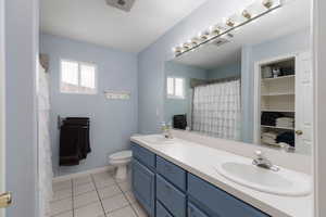 Full bath with double vanity, light tile patterned floors, and a shower with shower curtain