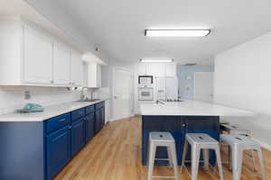 Kitchen with two tone cabinetry, a kitchen bar, a center island, light wood-style floors, and light stone countertops