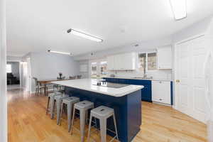 Kitchen with two tone cabinets, a center island, a breakfast bar, light wood-style floors, and white appliances