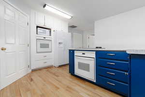 Kitchen featuring white appliances, blue cabinetry, light wood finished floors, and white cabinets