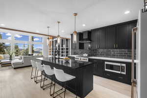Kitchen featuring dark cabinetry, a center island with sink, a kitchen breakfast bar, dark stone countertops, and fridge