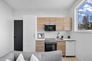 Kitchen featuring light wood finish cabinetry, modern cabinets, light stone counters, range with electric cooktop, and dishwasher