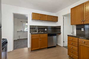 Kitchen featuring backsplash, stainless steel dishwasher, wood finish cabinets, and light wood finished floors.