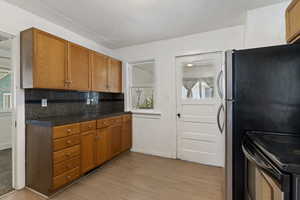 Kitchen featuring wood finish cabinetry, decorative backsplash, light wood-style floors, black electric range, and freestanding refrigerator