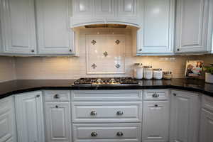 Kitchen featuring white cabinetry, dark stone countertops, stainless steel gas cooktop, and tasteful backsplash