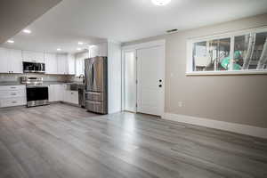 Kitchen with stainless steel appliances, white cabinets, recessed lighting, light wood-type flooring, and light stone countertops