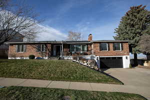 Ranch-style house with a chimney, brick siding, driveway, and an attached garage