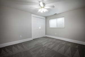 Unfurnished bedroom featuring dark colored carpet, ceiling fan, and a closet