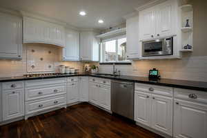 Kitchen with open shelves, white cabinets, stainless steel appliances, dark stone counters, and dark wood-style flooring