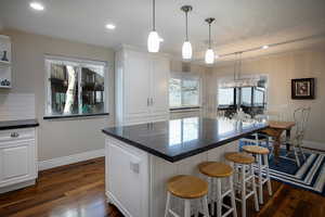 Kitchen with white cabinets, a kitchen bar, dark wood-style floors, and a kitchen island