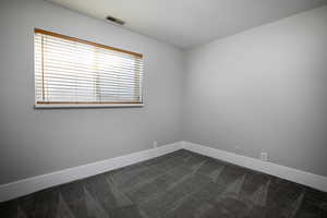 Spare room featuring dark colored carpet and baseboards
