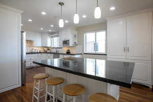 Kitchen with white cabinetry, a kitchen breakfast bar, decorative light fixtures, dark stone counters, and stainless steel appliances