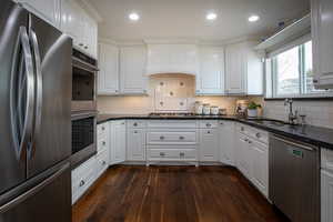 Kitchen featuring stainless steel appliances, white cabinetry, dark stone counters, dark wood-style flooring, and recessed lighting
