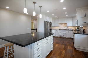 Kitchen featuring dark stone counters, white cabinetry, a breakfast bar, a center island, and dark wood finished floors
