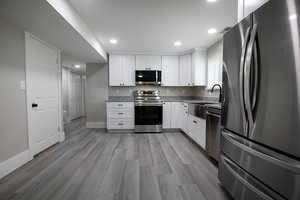 Kitchen featuring stainless steel appliances, white cabinetry, light stone countertops, light wood-style floors, and recessed lighting