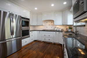 Kitchen with stainless steel appliances, dark stone counters, white cabinets, dark wood-style flooring, and recessed lighting