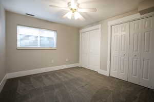Unfurnished bedroom with multiple closets, dark colored carpet, and ceiling fan