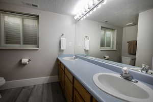 Full bath with double vanity, dark wood finished floors, and a textured ceiling